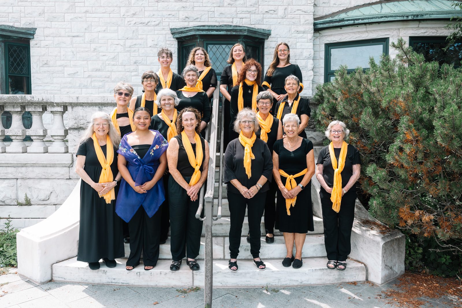 twc-sistersingers-group Singers from the Tucson Women's Chorus in black with gold scarves, on stone steps at Loyola University in Chicago